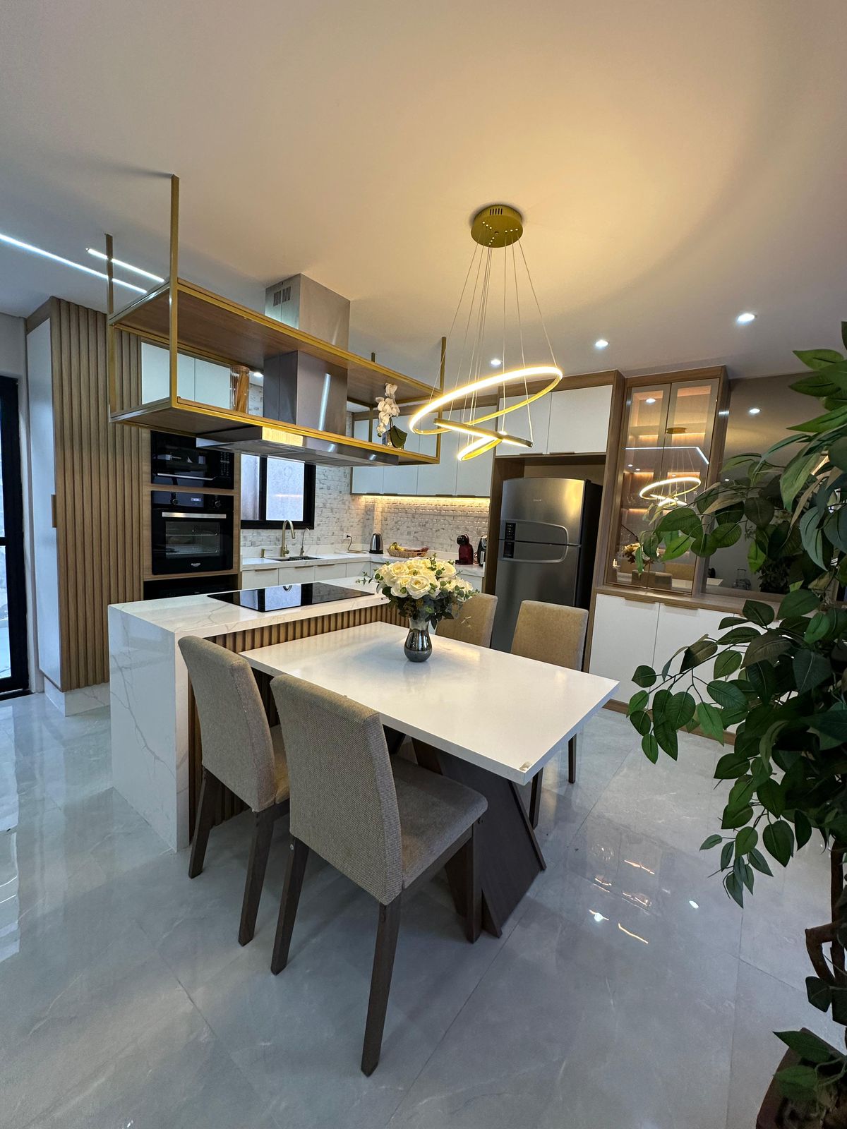 Cozinha planejada completa com mesa de jantar, ilha de mármore e lustre dourado – projeto Estillo Design São Paulo