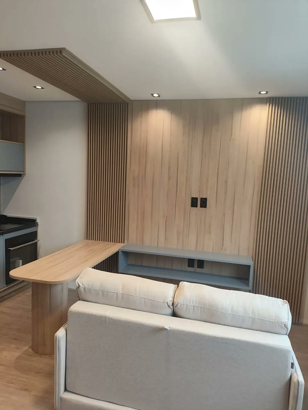 Sala compacta planejada com painel de TV ripado, bancada integrada e cozinha americana – apartamento Zona Leste SP Estillo Design